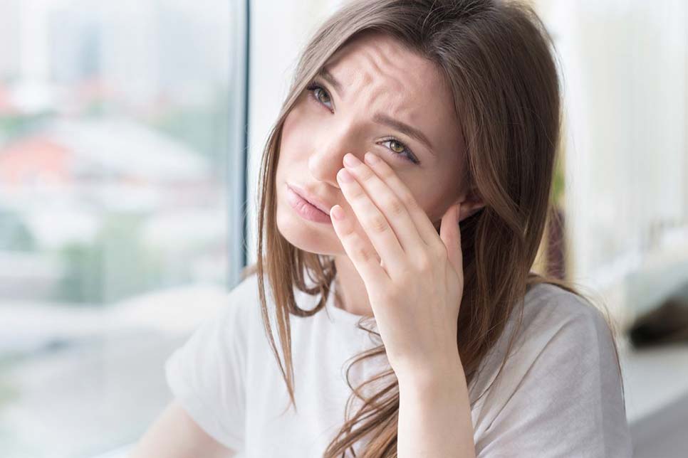 A woman itching her eyes in a white t shirt