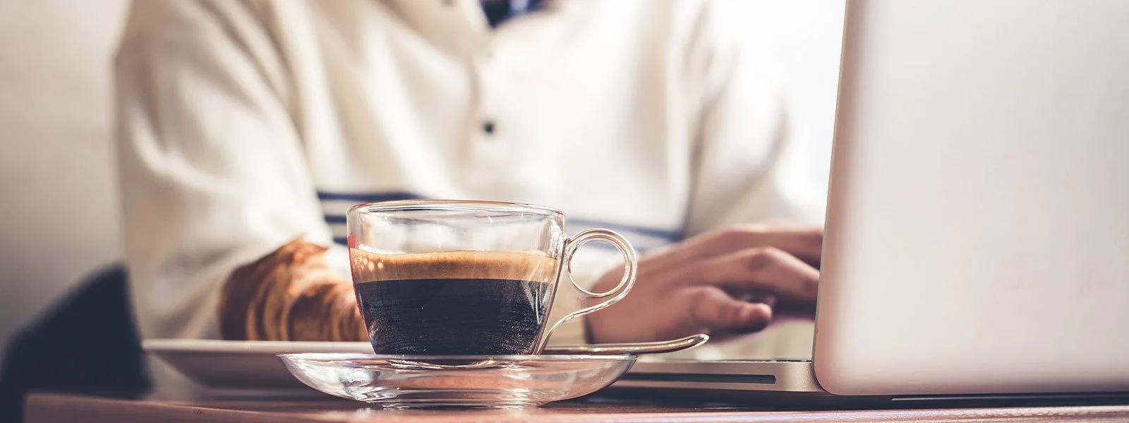 Coffee on a counter in front of a man working on a laptop