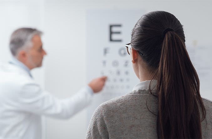 A girl reading from a list of letters far away with a doctor standing next to the poster