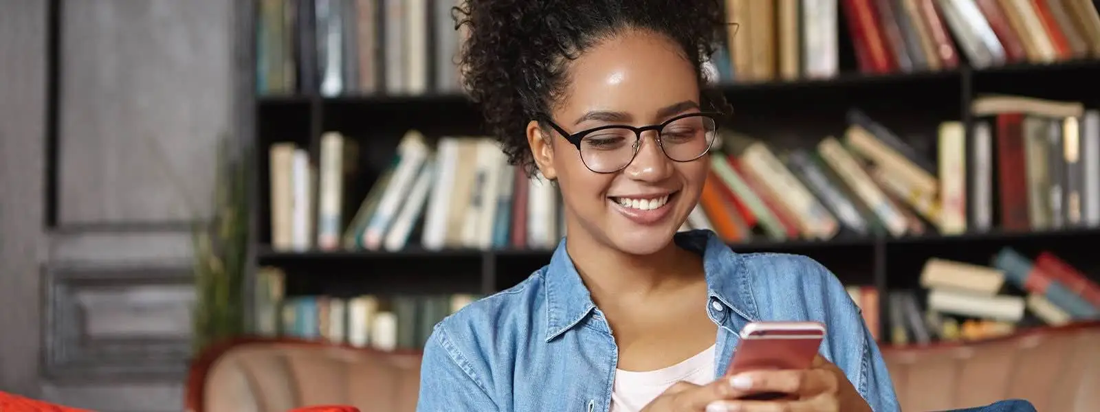 Young woman reading from her phone in front of a bookcase